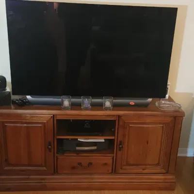Sale Photo Thumbnail #161: Large flat-screen television seated atop a traditional wooden media console with cabinets and open shelving, flanked by a pair of blue striped armchairs.