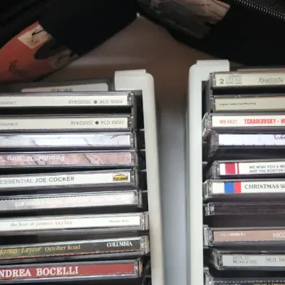 Sale Photo Thumbnail #86: Collection of compact discs in white plastic organizer racks, featuring titles by James Taylor, Andrea Bocelli, Neil Diamond, and various holiday albums.