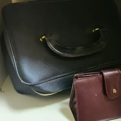 Sale Photo Thumbnail #67: Black structured vanity case or travel bag with gold-tone hardware alongside a vintage Etienne Aigner burgundy leather clutch wallet.