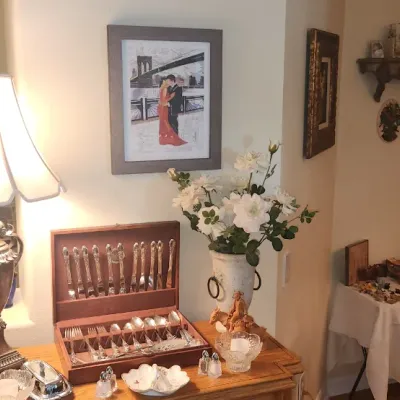 Sale Photo Thumbnail #2: Home decor collection including an ornate urn-style table lamp, framed artwork, and a wood silverware chest containing a flatware service.