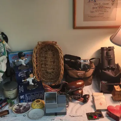 Sale Photo Thumbnail #296: Collection of tabletop decor and collectibles including a porcelain-headed clown doll, vintage cameras, binoculars, baseball bobbleheads, and a urn-form table lamp.