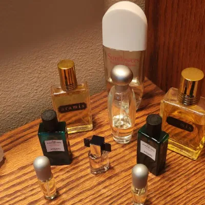 Sale Photo Thumbnail #97: Collection of vintage perfume and cologne bottles, including Aramis, Hermès, Elizabeth Arden Sunflowers, and miniature fragrance bottles displayed on a wooden surface.