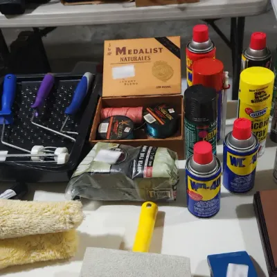 Sale Photo Thumbnail #384: Assortment of painting and household supply items, including aerosol spray cans, paint rollers, trays, and brushes.