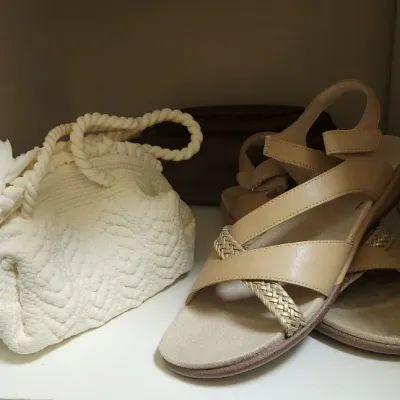 Sale Photo Thumbnail #66: A pair of women's tan leather strappy sandals alongside a white textured handbag with rope handles on a shelf.