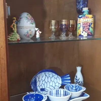 Sale Photo Thumbnail #155: Display cabinet filled with decorative collectibles, including a hand-painted floral porcelain egg, gold-rimmed glassware, a blue-and-white fish-shaped server set, and small southwestern figurines.