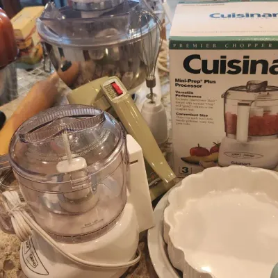 Sale Photo Thumbnail #237: Collection of kitchen items including a Cuisinart Mini-Prep Plus Processor, copper-colored bundt pan, vintage electric hand mixer, pie dish, and stand mixer accessories.