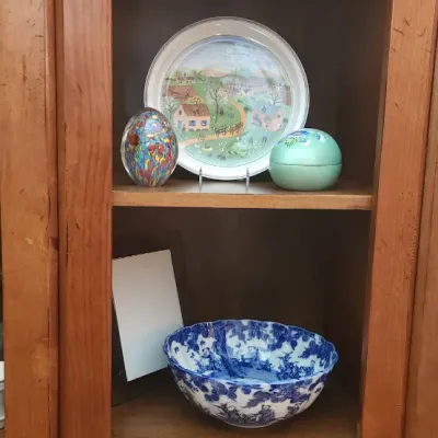 Sale Photo Thumbnail #154: Tall pine shelf unit displaying assorted decorative collectibles, including an art glass paperweight, a vintage painted landscape plate, a blue and white transferware bowl, and a glass decanter.