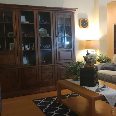 Sale Photo Thumbnail #157: Living room setup featuring a large dark wood display cabinet, a light gray sectional sofa, a wooden coffee table, and a blue pinstripe armchair.