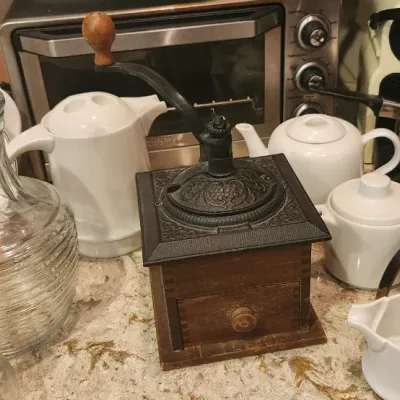 Sale Photo Thumbnail #216: Collection of kitchen items featuring a vintage manual coffee grinder, ceramic teapots, glassware decanters, stainless steel pitchers, and small countertop appliances.
