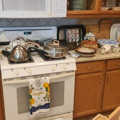 Sale Photo Thumbnail #221: Kitchen counter filled with various housewares, including stainless steel cookware, kettles, ceramic serving platters, baking pans, and small appliances.