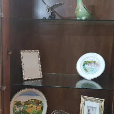 Sale Photo Thumbnail #152: Wooden display cabinet filled with decorative collectibles, including hand-painted porcelain plates, photo frames, bird figurines, a crystal bowl, and a miniature lute.