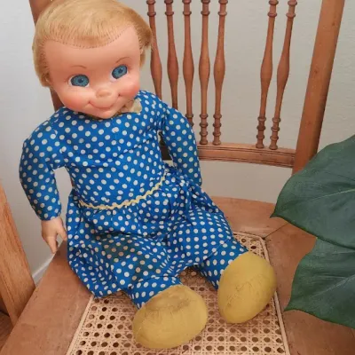 Sale Photo Thumbnail #266: Vintage 1960s Mattel Chatty Cathy doll wearing a blue polka-dot dress, seated on a wooden cane-seat chair.