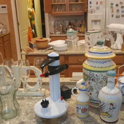 Sale Photo Thumbnail #205: Kitchenware collection featuring hand-painted Italian Deruta ceramics, stemless wine glasses, a wine opener, and a decorative oil and vinegar jar.