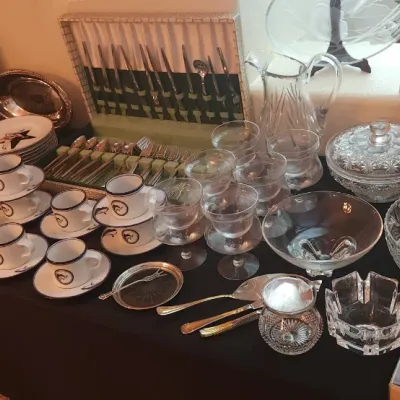 Sale Photo Thumbnail #12: Collection of crystal glassware, silver-plated serving pieces, fine china teacups, and a boxed flatware set displayed on a table.
