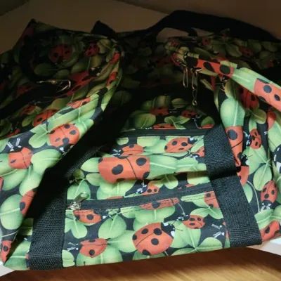 Sale Photo Thumbnail #74: Large duffle bag featuring a vibrant ladybug and green leaf print, complete with black nylon handles and zippered pockets.