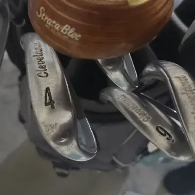 Sale Photo Thumbnail #349: Selection of Cleveland irons and a MacGregor Strata-Bloc wood club resting in a golf bag.