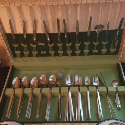 Sale Photo Thumbnail #13: Vintage mid-century stainless steel flatware set in a faux-alligator storage chest, displayed alongside silver-plated serving trays and cut glass tableware.