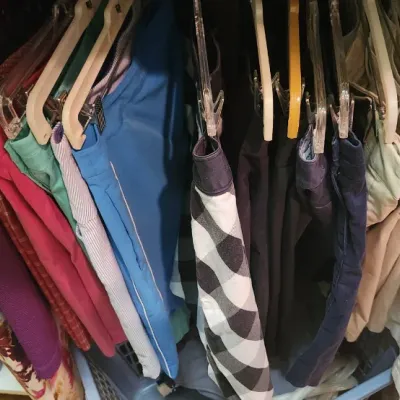 Sale Photo Thumbnail #62: Closet rack filled with a variety of men's and women's pants and shorts, including khaki, colorful athletic, and patterned styles on plastic hangers.