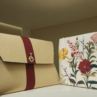 Sale Photo Thumbnail #70: Two contemporary women's handbags displayed on a shelf, featuring a beige envelope clutch with a red stripe and a Steve Madden floral print chain-strap shoulder bag.
