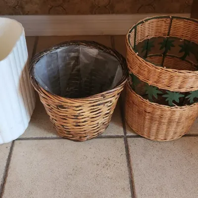 Sale Photo Thumbnail #124: Set of four wastebaskets and planters, including a white fluted plastic bin, a plastic-lined woven basket, and two stacked rattan baskets with palm leaf accents.
