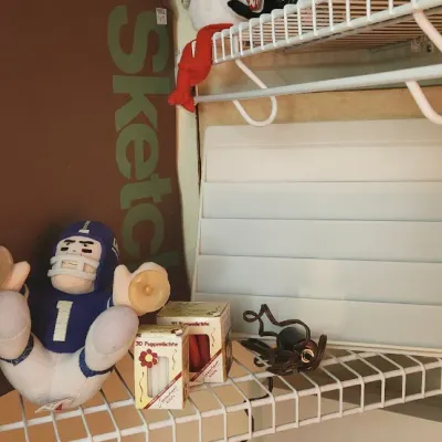 Sale Photo Thumbnail #292: Assorted closet shelf items including a spiral-bound sketchbook, a plush football player window toy, small boxed candles, and art supplies.