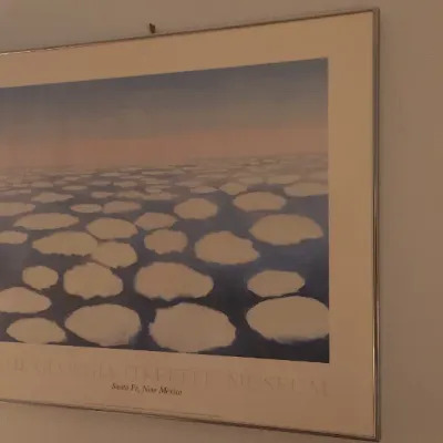 Sale Photo Thumbnail #182: Framed Georgia O'Keeffe Museum exhibition poster featuring her 'Sky Above Clouds IV' artwork, presented in a simple metal frame.