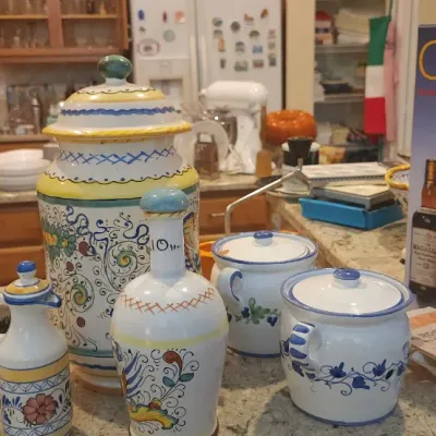 Sale Photo Thumbnail #206: Assortment of hand-painted Italian ceramic jars, decanters, and kitchenware alongside a 'Culinaria' book and a wine opener.