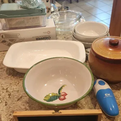 Sale Photo Thumbnail #236: Collection of kitchen items including a brown glazed stoneware bean pot, ceramic serving bowls, a vegetable chopper in box, and a boxed steak knife set.
