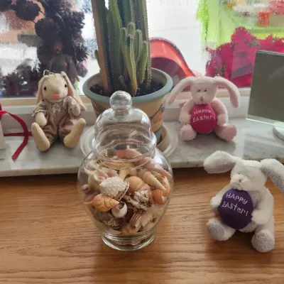 Sale Photo Thumbnail #274: Collection of tabletop decor including a glass jar filled with seashells, stuffed plush Easter bunnies, books, and small figurines.