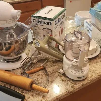Sale Photo Thumbnail #238: Collection of kitchen small appliances and baking tools, including a white KitchenAid stand mixer, Cuisinart Mini-Prep food processor, vintage hand mixer, wooden rolling pin, and bundt pan.