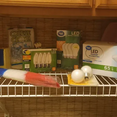 Sale Photo Thumbnail #247: Assorted household supplies including Great Value LED light bulb packs, cleaning brushes, a duster, a Spontex sponge, and cheesecloth displayed on a wire shelf.