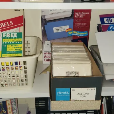 Sale Photo Thumbnail #282: Assorted office and stationery supplies, including Avery laser labels, Herald ivory envelopes, and Hewlett Packard inkjet paper organized on a white shelf.
