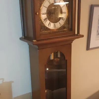 Sale Photo Thumbnail #24: Traditional wooden grandfather clock featuring a swan-neck pediment, brass-tone clock face with Roman numerals, and a glass pendulum display case.