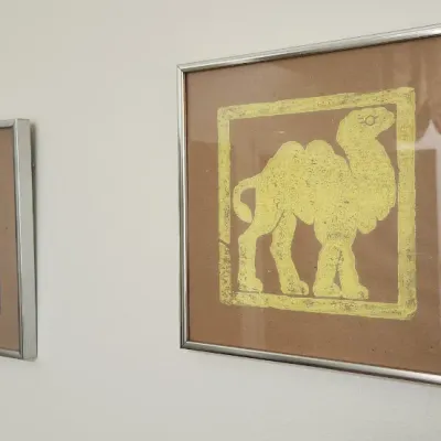 Sale Photo Thumbnail #279: Pair of framed mid-century animal linocut prints featuring a blue teddy bear and a yellow camel in simple silver-toned metal frames.