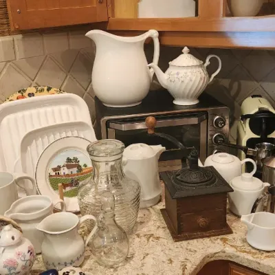 Sale Photo Thumbnail #215: Collection of kitchen items including a manual coffee grinder, various ceramic pitchers, teapots, serving platters, and espresso makers displayed on a granite countertop.