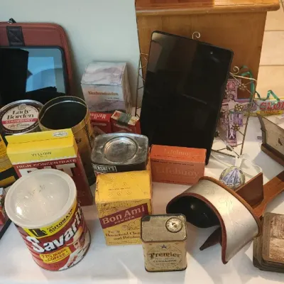 Sale Photo Thumbnail #143: Collection of vintage advertising tins, boxes, and household items alongside modern electronics, including a Savarin coffee tin, Bon Ami powder, an antique stereoscope viewer with cards, and an Amazon Kindle.
