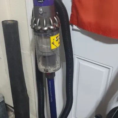 Sale Photo Thumbnail #357: Dyson Cyclone V10 Absolute cordless stick vacuum with attached hose extension, displayed near a water heater.