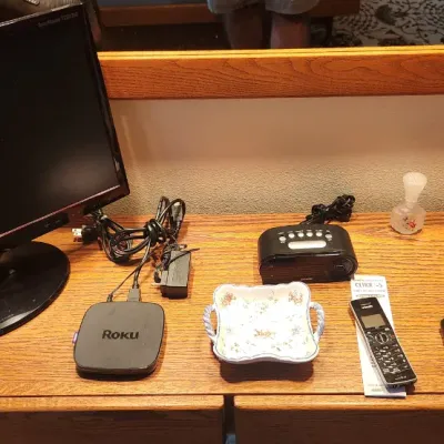 Sale Photo Thumbnail #101: Collection of tabletop electronics and personal items, including a Samsung computer monitor, Roku streaming player, digital alarm clock, landline phone handset, leather wallets, and various perfume and cologne bottles.