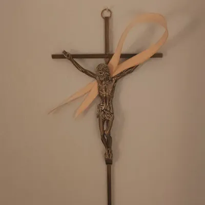 Sale Photo Thumbnail #175: Metal wall crucifix, featuring a detailed figure of Jesus and adorned with a light peach ribbon.