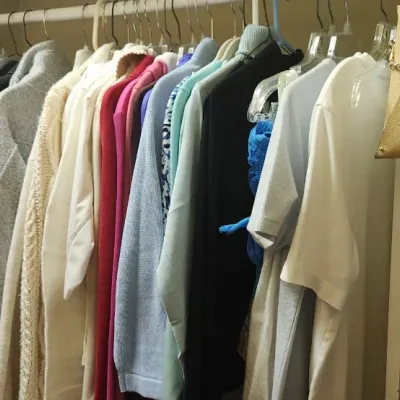 Sale Photo Thumbnail #76: Walk-in closet stocked with women's apparel, featuring assorted coats, sweaters, and tops on hangers alongside handbags on upper and lower shelves.