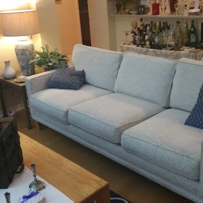 Sale Photo Thumbnail #148: Contemporary light gray upholstery three-cushion sofa paired with blue patterned throw pillows, shown in a furnished living room setting.