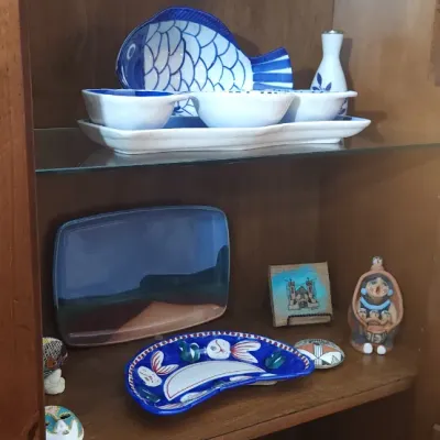 Sale Photo Thumbnail #156: Collection of decorative ceramic serverware and art pieces, including blue and white fish-shaped platters, small pottery figurines, and glassware inside a wooden display cabinet.