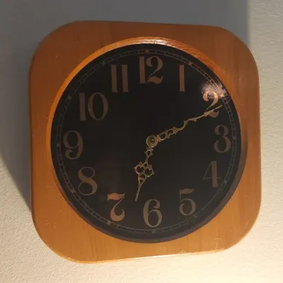 Sale Photo Thumbnail #150: Mid-century wall clock featuring a square wooden frame with rounded corners, a black face, and ornate gold-toned hands.