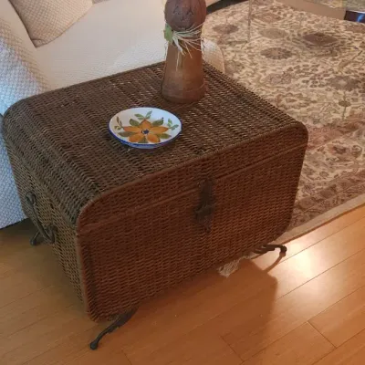 Sale Photo Thumbnail #19: Dark woven wicker trunk-style end table featuring wrought iron legs and side handles, topped with decor.