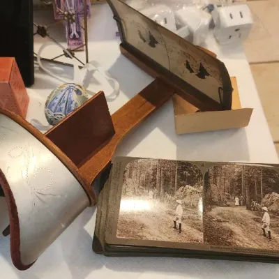 Sale Photo Thumbnail #144: Antique wooden and metal stereoscope viewer shown alongside a stack of stereograph photo cards and vintage advertising tins.
