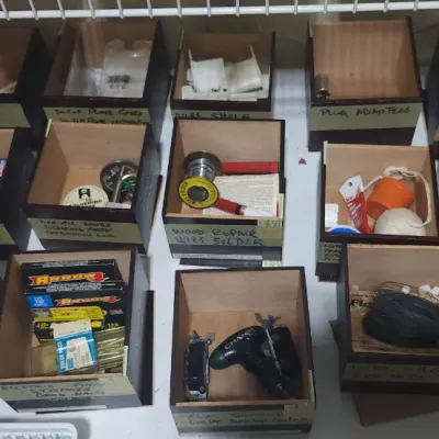 Sale Photo Thumbnail #354: Collection of organized wooden storage bins filled with various hardware, tools, solder, and household supplies, each labeled with handwritten tape.