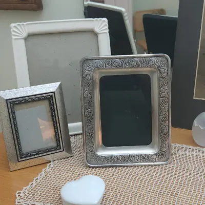 Sale Photo Thumbnail #301: Collection of decorative picture frames including embossed metal and white molded designs, displayed alongside frosted glass cracked-egg figurines and a heart-shaped trinket box.