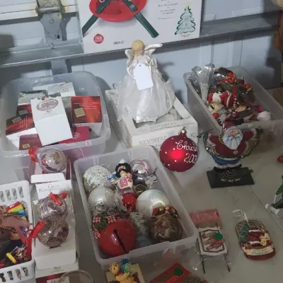 Sale Photo Thumbnail #337: Table displaying an assortment of Christmas decor items, including holiday ornaments in plastic storage tubs, boxed ornaments, figurines, and patterned gift boxes.