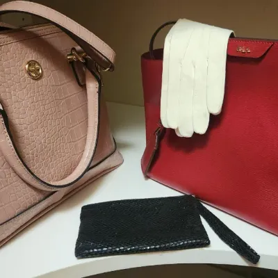 Sale Photo Thumbnail #72: Collection of women's fashion accessories including a blush pink croc-embossed satchel, a red Ralph Lauren tote bag, a small black snakeskin pouch, and a pair of white dress gloves.