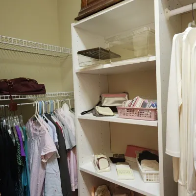 Sale Photo Thumbnail #49: Walk-in closet containing assorted women's clothing, straw hats, small handbags, and a white laminate shelving unit.